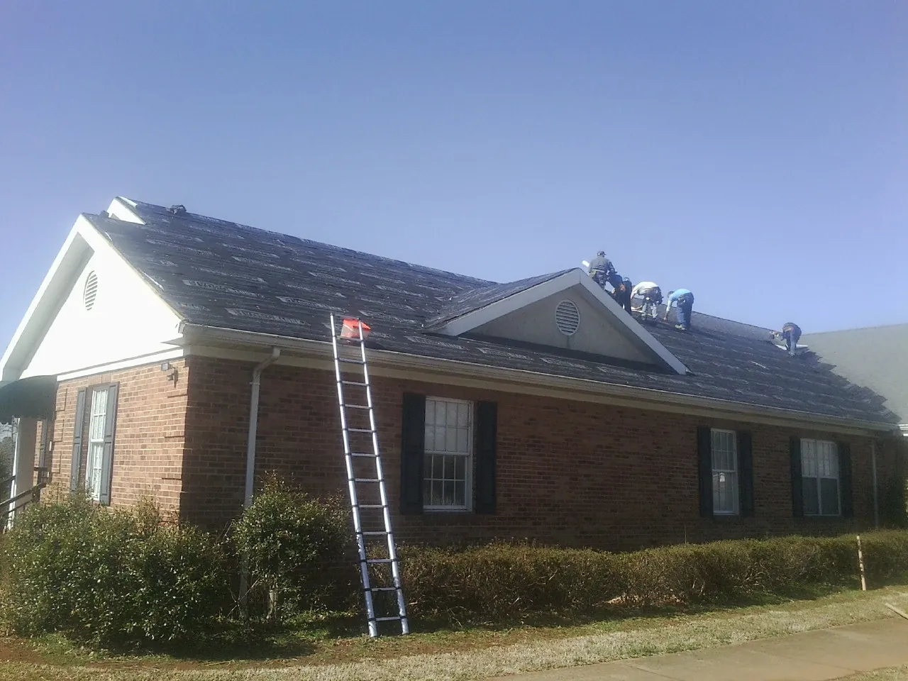 Crew tearing shingles off a brick ranch roof with a ladder set — Emergency Roof Repair work by our crew in Rockwell