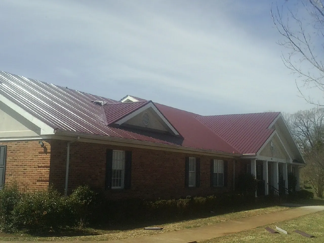 Red metal roof with gabled entries on a long brick building, from a Hail Damage Roof Repair job in Rockwell
