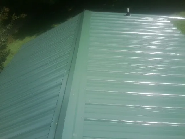 New green metal panels meeting at the ridge of a roof — Flat Roof Repair work by our crew in Rockwell