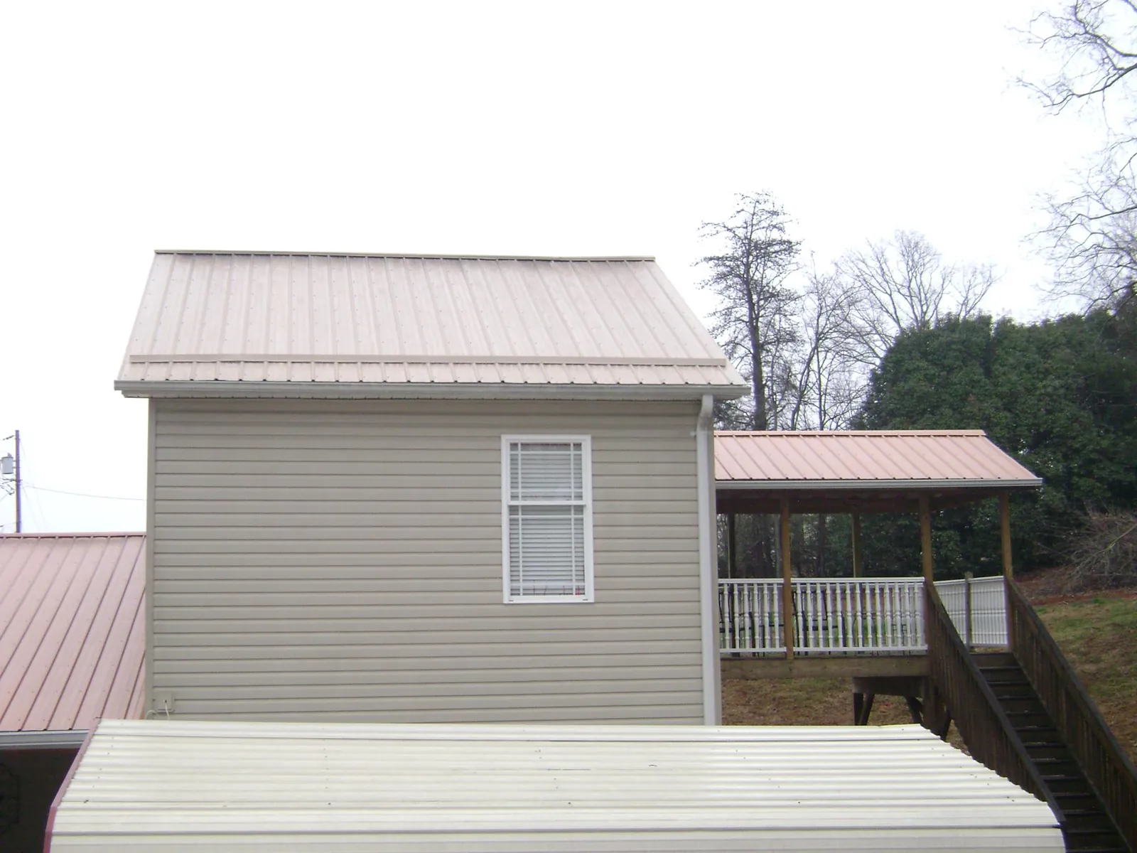Tan metal roofs on a two story addition and attached porch, from a Roof Replacement job in Rockwell